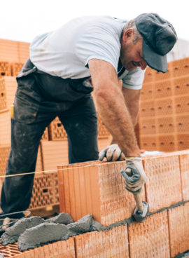 industrial worker building exterior walls, using hammer for laying bricks in cement. Detail of worker with tools and concrete