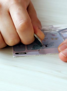 A hand scratching an instant lottery with coins.