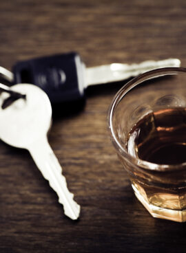 A glass of whisky and a set of car keys on a wooden table